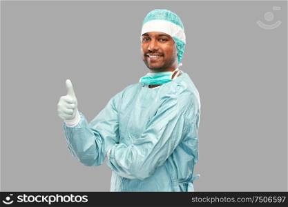 medicine, surgery and people concept - smiling indian male doctor or surgeon in protective wear showing thumbs up over grey background. indian male doctor or surgeon showing thumbs up