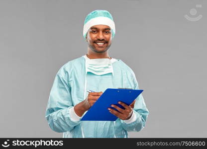 medicine, surgery and people concept - smiling indian male doctor or surgeon in protective wear with clipboard over grey background. indian male doctor or surgeon with clipboard