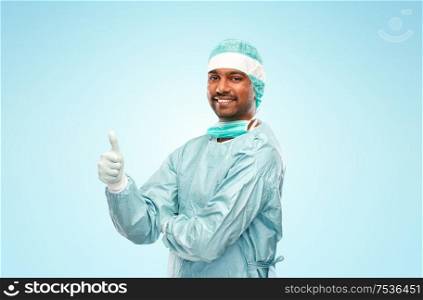 medicine, surgery and people concept - smiling indian male doctor or surgeon in protective wear showing thumbs up over blue background. indian male doctor or surgeon showing thumbs up