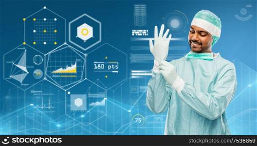 medicine, surgery and people concept - smiling indian male doctor or surgeon in protective wear putting glove over virtual charts projection on blue background. indian male doctor or surgeon putting glove on