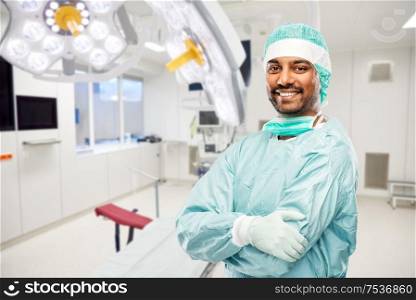 medicine, surgery and people concept - smiling indian male doctor or surgeon in protective wear over operating room in hospital background. smiling indian male doctor or surgeon at hospital