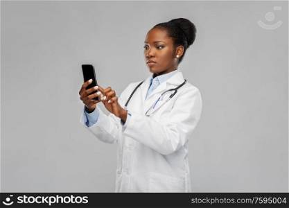 medicine, technology and healthcare concept - african american female doctor or in white coat with smartphone and stethoscope over background. african american female doctor with smartphone