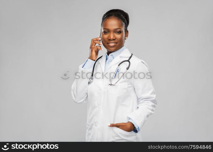 medicine, technology and healthcare concept - happy smiling african american female doctor or in white coat with stethoscope calling on smartphone over background. african female doctor calling on smartphone