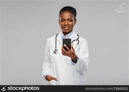 medicine, technology and healthcare concept - happy smiling african american female doctor or in white coat with smartphone and stethoscope over background. african american female doctor with smartphone