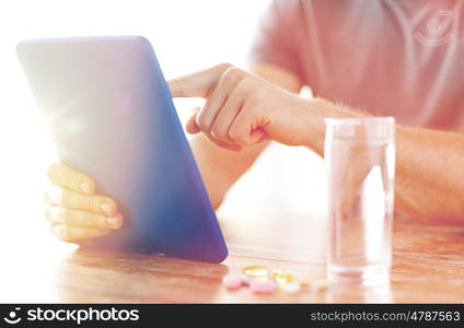 medicine, technology, nutritional supplements and people concept - close up of male hands with tablet pc computer, pills and water on table