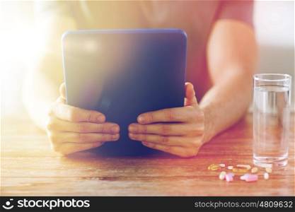 medicine, technology, nutritional supplements and people concept - close up of male hands with tablet pc computer, pills and water on table