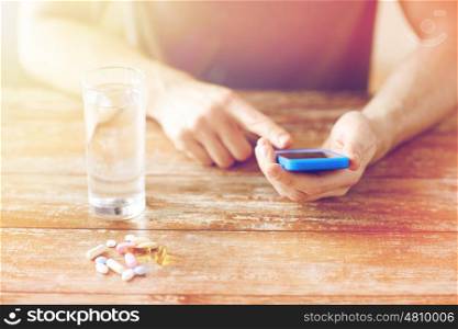 medicine, technology, nutritional supplements and people concept - close up of male hands smartphone, pills and water on table