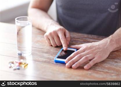 medicine, technology, nutritional supplements and people concept - close up of male hands pointing finger to blank smartphone screen, pills and water on table
