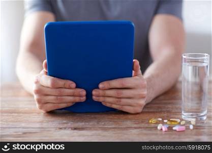 medicine, technology, nutritional supplements and people concept - close up of male hands with tablet pc computer, pills and water on table