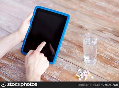medicine, technology, nutritional supplements and people concept - close up of male hands pointing finger to blank tablet pc computer screen, pills and water on table