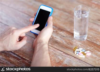 medicine, technology, nutritional supplements and people concept - close up of male hands pointing finger to blank smartphone screen, pills and water on table
