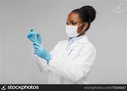 medicine, vaccination and healthcare concept - african american female doctor or scientist in mask with syringe over grey background. african american female doctor with syringe