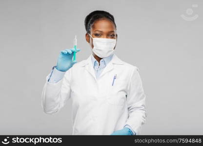 medicine, vaccination and healthcare concept - african american female doctor or scientist in mask with syringe over grey background. african american female doctor with syringe