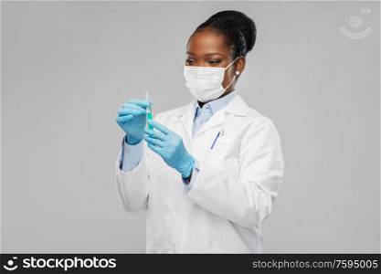 medicine, vaccination and healthcare concept - african american female doctor or scientist in mask with syringe over grey background. african american female doctor with syringe