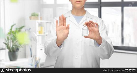 medicine, vaccination and healthcare concept - close up of female doctor or nurse with drug in bottle showing stop gesture over medical office at hospital background. doctor with syringe shows stop gesture at hospital