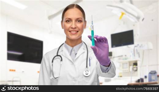 medicine, vaccination and healthcare concept - close up of happy smiling female doctor with stethoscope and syringe over hospital background. female doctor with medicine in syringe at hospital