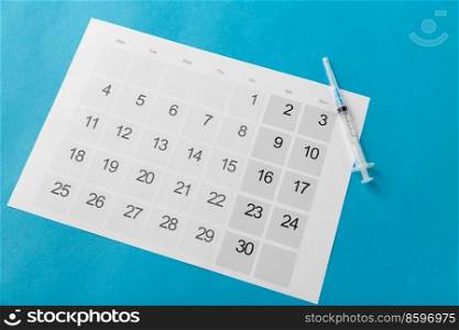 medicine, vaccination and healthcare concept - disposable syringe and calendar on blue background. disposable syringe and calendar on blue background