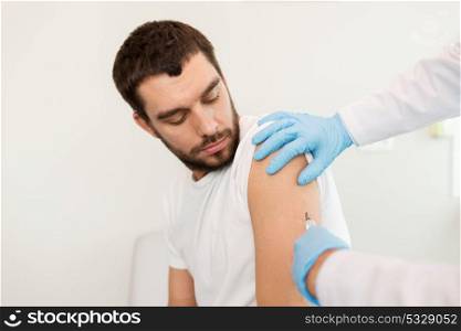 medicine, vaccination and healthcare concept - doctor or nurse hands with syringe doing injection of vaccine to male patient. male patient and doctor hands with syringe