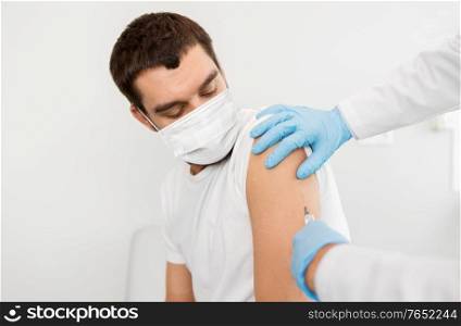 medicine, vaccination and healthcare concept - doctor or nurse&rsquo;s hands with syringe doing injection of vaccine to male patient wearing face protective medical mask for protection from virus disease. male patient in mask and doctor hands with syringe