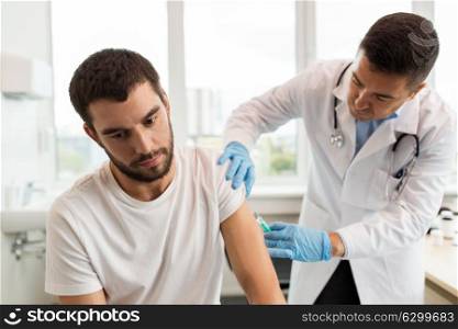 medicine, vaccination and healthcare concept - doctor or nurse with syringe doing injection of vaccine to male patient. patient and doctor with syringe doing injection