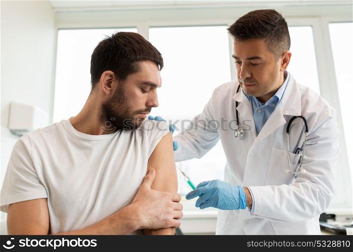 medicine, vaccination and healthcare concept - doctor with syringe doing injection of vaccine to male patient. patient and doctor with syringe doing vaccination