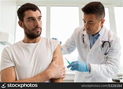 medicine, vaccination and healthcare concept - doctor with syringe doing injection of vaccine to male patient. patient and doctor with syringe doing vaccination