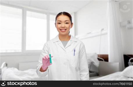 medicine, vaccination and healthcare concept - happy smiling asian female doctor or nurse with syringe over hospital ward background. asian female doctor with syringe at hospital