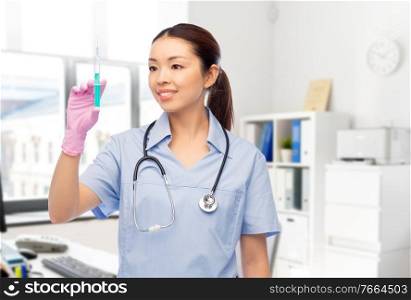 medicine, vaccination and healthcare concept - happy smiling asian female doctor or nurse in blue uniform with stethoscope and syringe over hospital background. happy asian female nurse with syringe at hospital