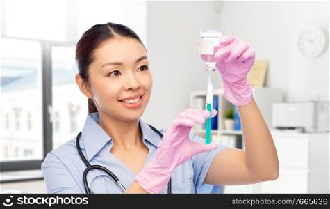 medicine, vaccination and healthcare concept - happy smiling asian female doctor or nurse in blue uniform with stethoscope and syringe over hospital background. happy asian female nurse with medicine and syringe