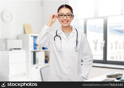 medicine, vision and healthcare concept - happy smiling asian female doctor in glasses and white coat over hospital background. happy asian female doctor in glasses at hospital