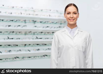 medicine, vision and healthcare concept - happy smiling female eye doctor or ophthalmologist in white coat over glasses at optical store background. happy smiling female doctor at optical store
