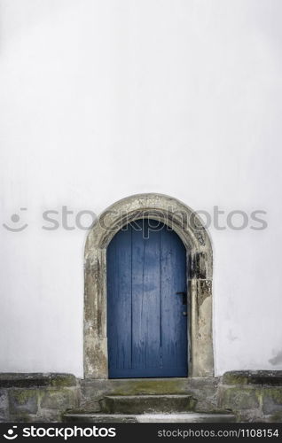 Medieval arched door. Aged wooden door in blue color with stone stairs and white wall. Just one door and an empty white house wall. Old blue entrance.