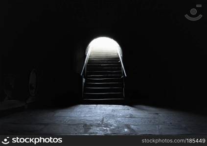 Medieval basement in complete darkness with a strong light at the exit
