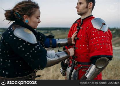 Medieval knight helps his friend to put on armor, great tournament. Armored ancient warrior in armour posing in the field. Medieval knight helps his friend to put on armor