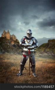 Medieval knight in armor and helmet against castle. Armored ancient warrior in armour in the field. Knight in armor and helmet