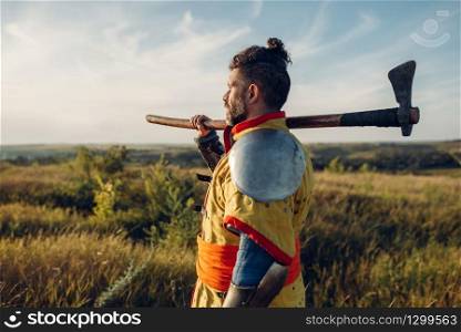 Medieval knight with axe poses in armor opposite the castle, great combat. Armored ancient warriors in armour posing in the field. Medieval knight with axe poses in armor
