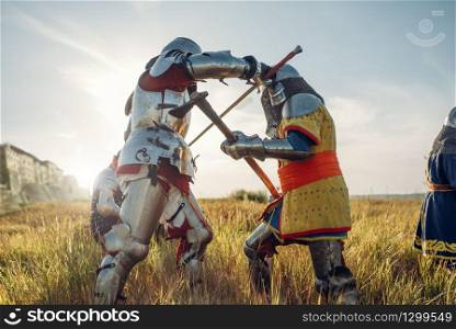 Medieval knights in armor and helmets fight with sword and axe. Armored ancient warrior in armour posing in the field