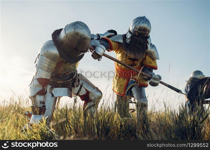 Medieval knights in armor and helmets fight with sword and axe. Armored ancient warrior in armour posing in the field. Medieval knights fight with sword and axe