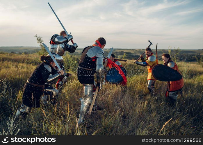 Medieval knights in armor and helmets fight with sword and axe. Armored ancient warrior in armour posing in the field. Medieval knights fight with sword and axe