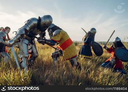 Medieval knights in armor and helmets fight with sword and axe, great battle. Armored ancient warrior in armour posing in the field