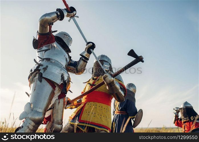 Medieval knights in armor and helmets fight with sword and axe, great battle. Armored ancient warrior in armour posing in the field. Medieval knights fight, great battle