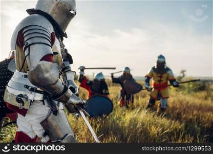 Medieval knights in armor and helmets fight with sword and axe, great battle. Armored ancient warrior in armour posing in the field. Medieval knights fight, great battle