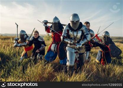 Medieval knights in armor and helmets fight with sword and axe, great tournament. Armored ancient warrior in armour posing in the field
