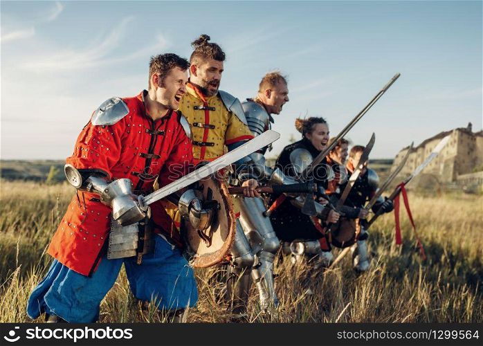 Medieval knights in armor and helmets standing in a row before battle. Armored ancient warrior in armour posing in the field