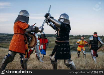 Medieval knights in armour and helmets fight with swords. Armored ancient warriors posing in the meadow. Knights in armour and helmets fight with swords