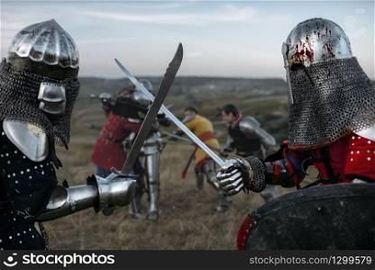 Medieval knights in armour and helmets fight with swords. Armored ancient warriors posing in the meadow. Knights in armour and helmets fight with swords