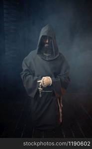 Medieval monk holds wooden cross in hands and praying, religion. Mysterious friar in dark cape. Mystery and spirituality