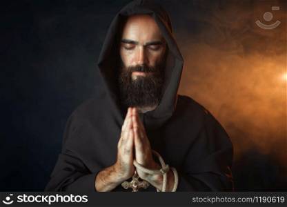 Medieval monk in black robe with hood praying with closed eyes, secret ritual. Mysterious friar in dark cape. Medieval monk praying with closed eyes