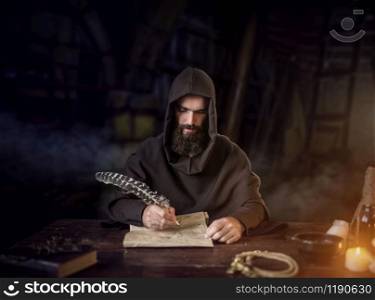 Medieval monk in robe and hood writes with a goose feather, black background, secret ritual. Mysterious friar in dark cape. Mystery and spirituality. Medieval monk in robe writes with a goose feather