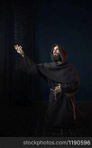 Medieval monk kneeling and praying, religion. Mysterious friar in dark cape, Mystery and spirituality
